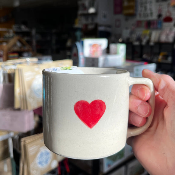 A ceramic mug with a bright reddish pink heart printed in the middle is held up from the right side of the image. 