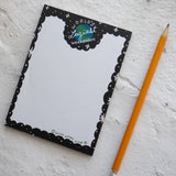 Small notebook with black border reads 'World's laziest workaholic' with a pencil lying alongside