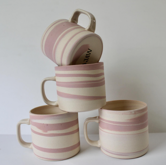Pile of off-white ceramic mugs with uneven pink stripes wrapping around each.