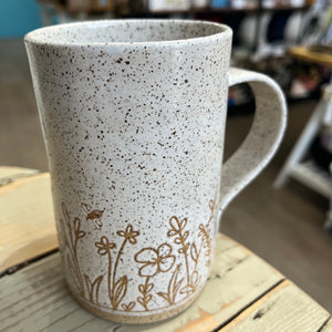 A speckled ceramic mug in white clay with carved flower designs