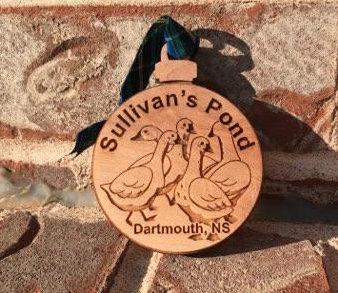 A close up photo of a laser etched round wooden ornament with 5 geese engraved on the front. Bold text reads Sullivan's Pond - Dartmouth NS