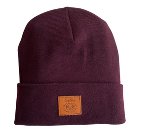 Three toques lay flat on a white background, green, beige and burgundy. All have a square leather patch reading "explore your home"